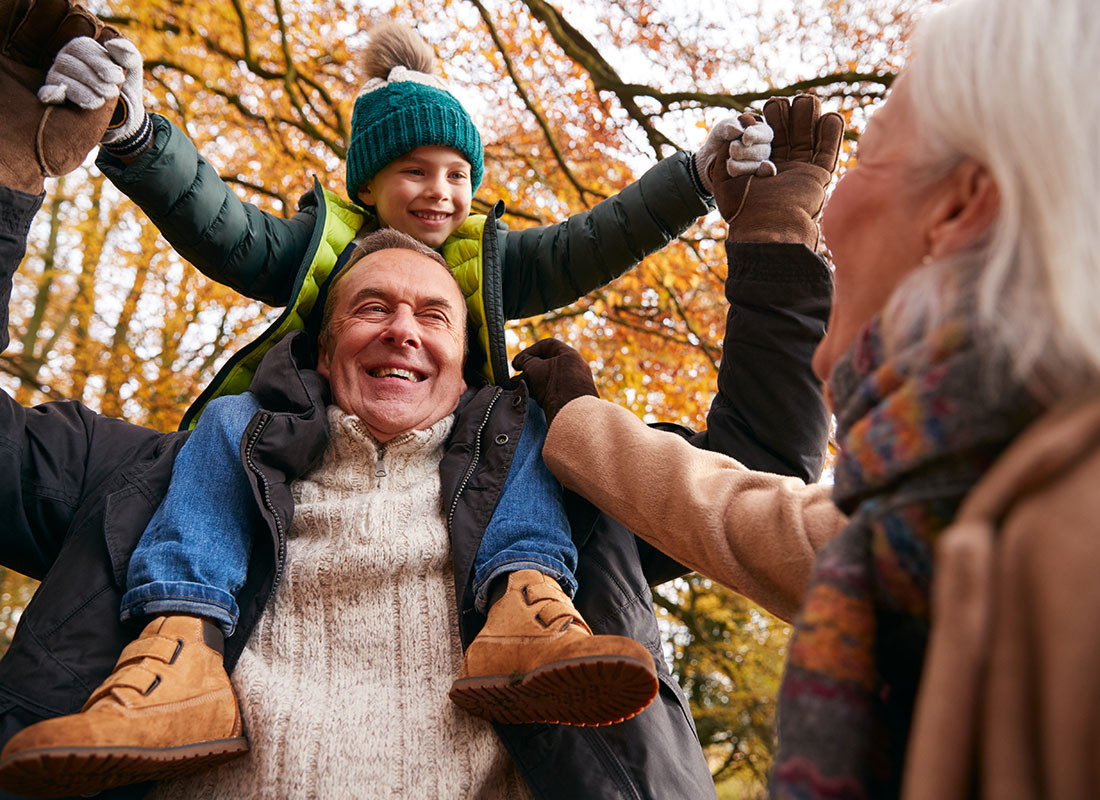 About Our Agency - Portrait of Cheerful Grandparents Having Fun Playing with Their Grandson While Walking in the Park on a Chilly Fall Day